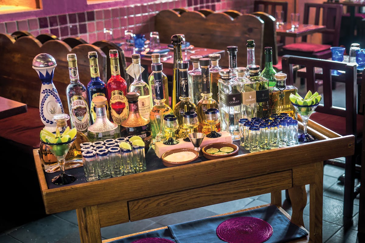 bar table with lots of tequila bottles, tequilla shots and lemons